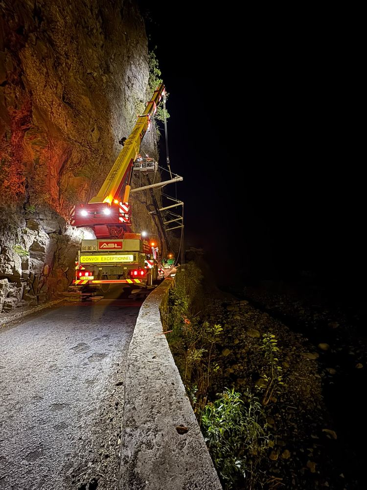 Grue mobile ASL de nuit sur une route étroite au pied d’une falaise